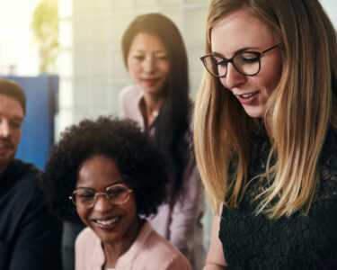 Smiling businesswoman standing in a modern office with a diverse group of work colleagues in the background