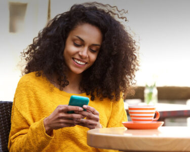 Close up portrait of beautiful young african american woman reading text message on mobile phone at coffee shop